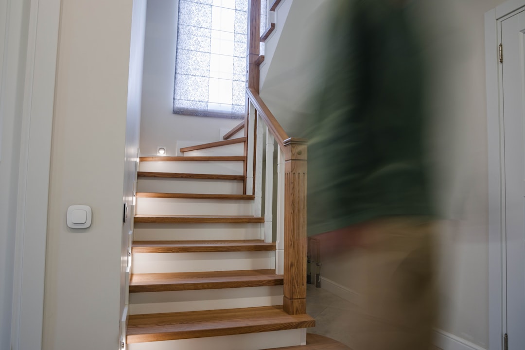 Blurred figure ascends wooden staircase indoors.