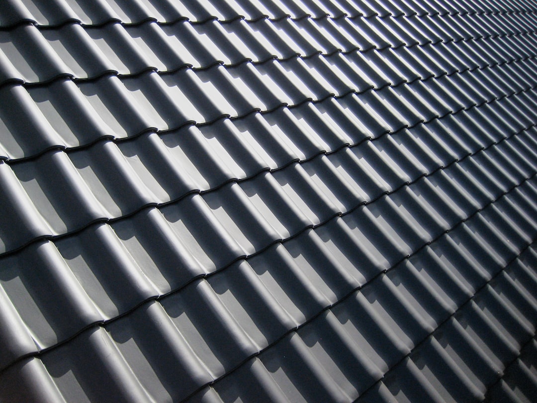 A pattern of dark grey roof tiles with sharp shadows in bright light